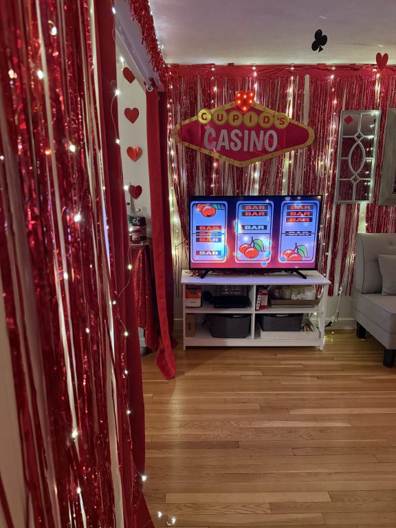 Casino Themed Dinner Party with red and gold decor with "Cupid's Casino" Sign and Slots on TV